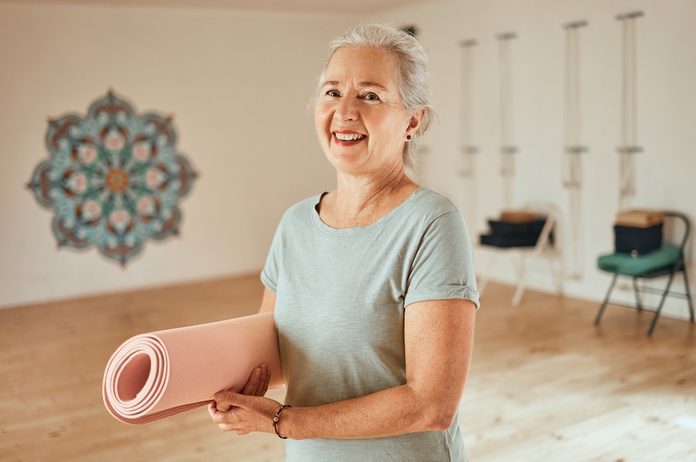 A smiling senior woman holding a yoga mat and getting ready for class