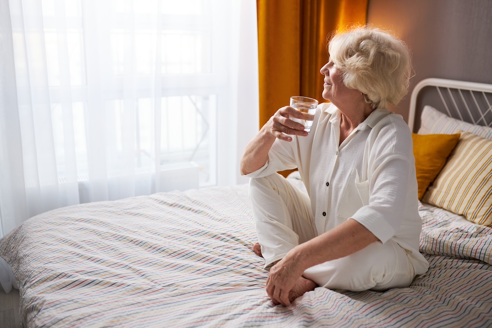 A happy senior woman wakes up well rested and drinking a glass of water